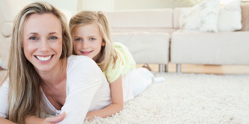 Mother lying on carpet with young daughter lying on her back on top
